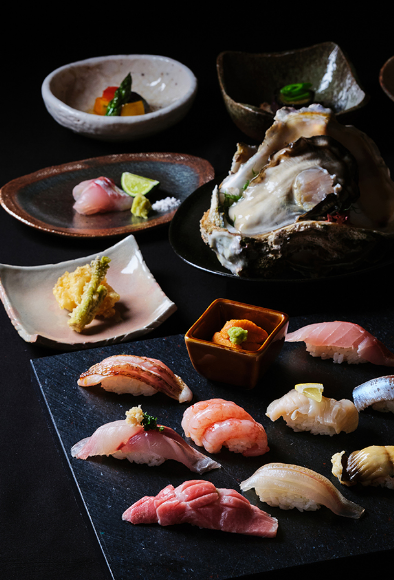 Various nigirizushi and Japanese dishes are beautifully presented on black plates. 