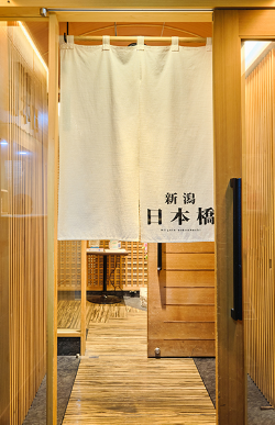 The wooden entrance to the sushi restaurant with a white curtain reading “Niigata Nihonbashi.