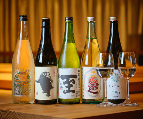 Five bottles and two wine glasses lined up on the counter.