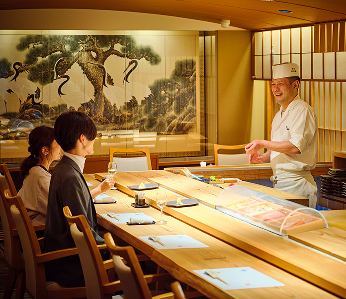 寿司店のカウンターで、寿司職人と会話を楽しむお客様。