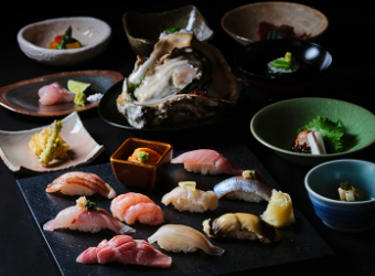 Sushi and sashimi of various kinds and small dishes arranged on a black table are beautifully presented.