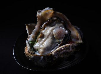 Large raw oysters served on a black plate.