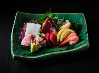 An assortment of fresh sashimi served on green ceramic plates.Shrimp, tuna, squid, etc. are lined up.