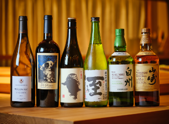 Six bottles of alcoholic beverages lined up on the counter.They include wine, sake, and whiskey.