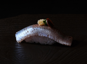 Sardine nigirizushi served on a black plate.