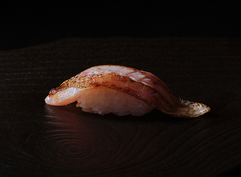 Seared salmon nigirizushi served on a black plate.